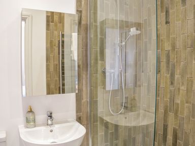 A bathroom with a sink and mirror beside a shower with glass door and tiled walls at Bryn Mor in Benllech