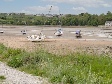 Several sailboats on a sandy and muddy shore with grass in the foreground and houses on green hills in the background at Bryn Mor in Benllech