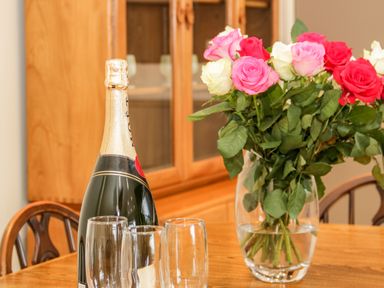 A dining table with a bottle of champagne three empty glasses and a vase of roses at Bryn Mor in Benllech