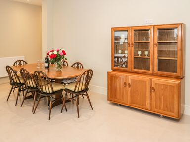 A dining room with a wooden table surrounded by chairs and a wooden cabinet with glass doors at Bryn Mor in Benllech