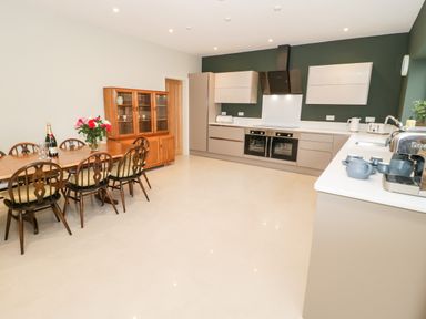 A kitchen with a wooden dining table and chairs a glass cabinet ovens and countertop appliances at Bryn Mor in Benllech