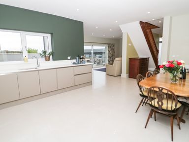 A kitchen and dining area with a table and chairs next to stairs and a living room area with a chair at Bryn Mor in Benllech