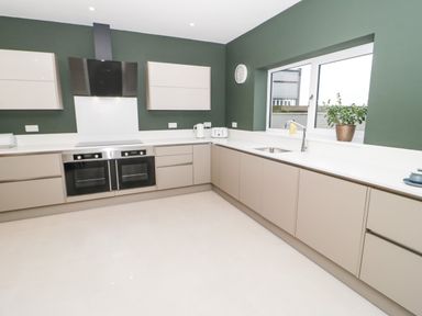 A kitchen with beige cabinets a stove double oven a stainless steel sink and a window with a plant on the sill at Bryn Mor in Benllech