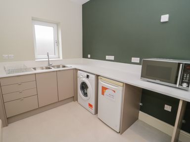 A kitchen with a double sink washing machine small fridge and microwave at Bryn Mor in Benllech