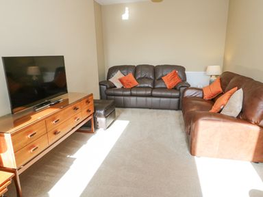 A living room with two leather sofas a wooden TV stand with a flat screen TV and a lamp at Bryn Mor in Benllech