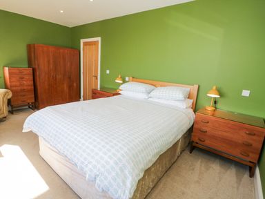 A bedroom with a large bed two bedside tables lamps a wardrobe a chest of drawers and an armchair at Bryn Mor in Benllech