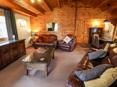 A living room with brown leather sofas a coffee table wooden walls and a dining table at Avocet Lodge in Tattershall Lakes Country Park