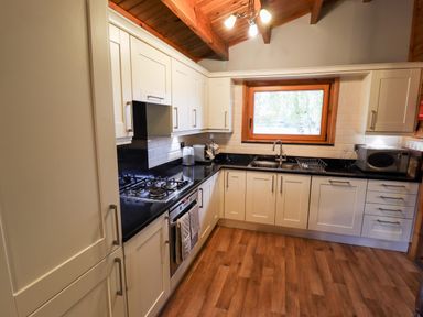 A kitchen with white cabinets black countertops a gas stove oven microwave and a window at Avocet Lodge in Tattershall Lakes Country Park