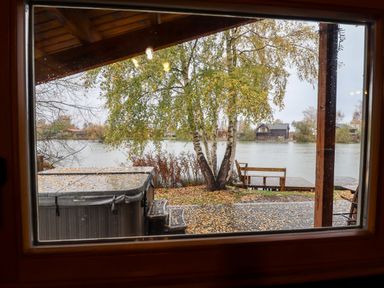 A view of a tree and a hot tub outside near a lake with houses in the distance at Avocet Lodge in Tattershall Lakes Country Park