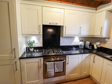 A kitchen with white cabinets black countertops a gas stove oven a plant toaster and coffee machine at Avocet Lodge in Tattershall Lakes Country Park