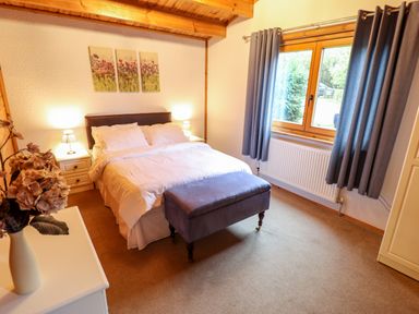 A bedroom with a double bed two bedside tables with lamps a window with curtains and a blue ottoman at Avocet Lodge in Tattershall Lakes Country Park