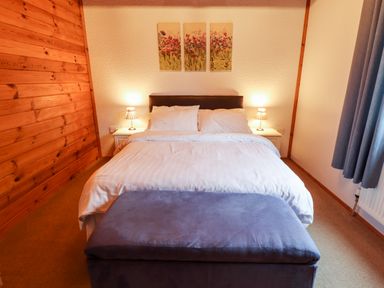 A bedroom with a double bed two bedside tables with lamps a blue ottoman and a three-panel floral artwork on the wall at Avocet Lodge in Tattershall Lakes Country Park