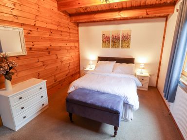 A bedroom with a double bed bedside tables a chest of drawers and a wooden wall at Avocet Lodge in Tattershall Lakes Country Park