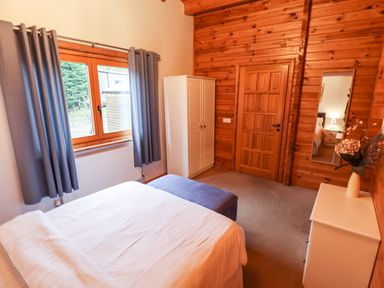 A bedroom with a bed and white dresser a mirror and a wardrobe with blue curtains at Avocet Lodge in Tattershall Lakes Country Park