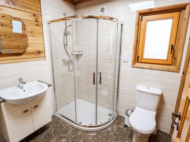 A bathroom with a curved glass shower enclosure a white sink with cabinet a toilet and a small frosted window at Avocet Lodge in Tattershall Lakes Country Park