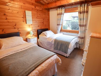 A bedroom with two beds a nightstand with a lamp a window with curtains and a chest of drawers at Avocet Lodge in Tattershall Lakes Country Park