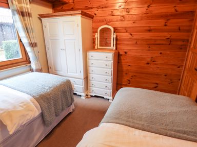 A bedroom with two single beds a white wardrobe a white chest of drawers with a mirror and a window at Avocet Lodge in Tattershall Lakes Country Park