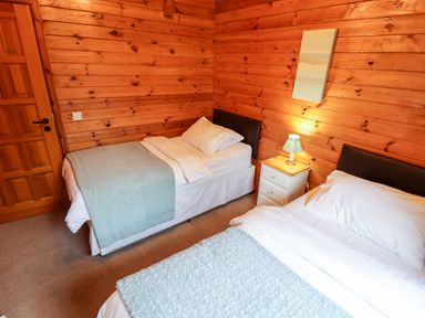 A bedroom with two single beds a nightstand with a lamp and wooden walls at Avocet Lodge in Tattershall Lakes Country Park