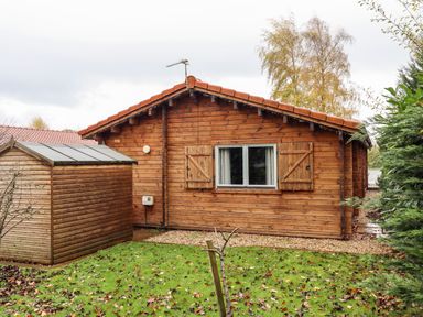 A wooden cabin with a small shed and a grassy yard at Avocet Lodge in Tattershall Lakes Country Park