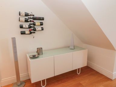 A white cabinet with items on top and wine bottles mounted on the wall in a room with wooden floor at 2 The Reformed Church in Embleton