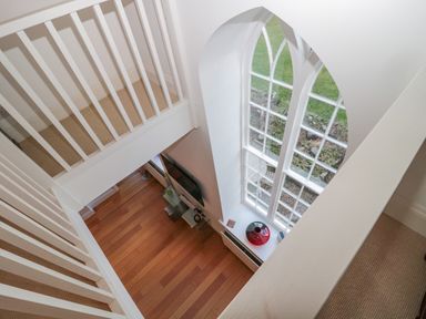 A view from an upper floor overlooking a room with wooden flooring and a large arched window at 2 The Reformed Church in Embleton
