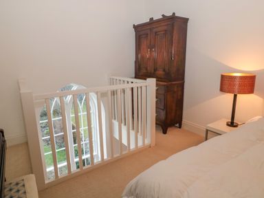 A bedroom corner with a wooden armoire a bedside table with lamp and a staircase railing at 2 The Reformed Church Embleton