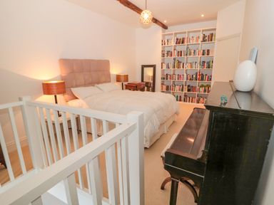 A bedroom with a bed two lamps a bookshelf a piano and a staircase railing at 2 The Reformed Church in Embleton