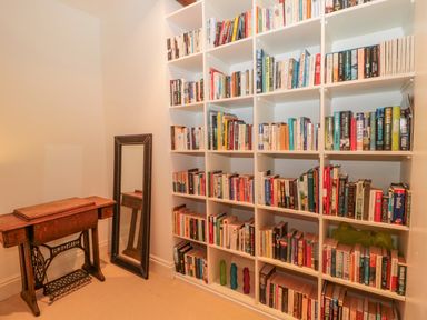 A room with a large white bookshelf filled with books a wooden sewing machine table and a standing mirror at 2 The Reformed Church Embleton