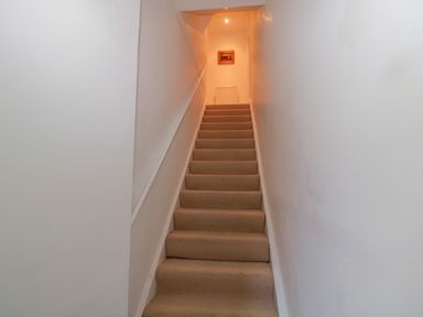 A staircase with beige carpet and white walls leading to a hallway with a radiator and framed picture at 2 The Reformed Church in Embleton