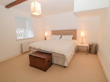 A bedroom with a bed a wooden chest two lamps a small table and a window at 2 The Reformed Church in Embleton