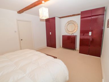 A bedroom with a white bedspread two red wardrobes a red chest of drawers and a circular mirror at 2 The Reformed Church in Embleton