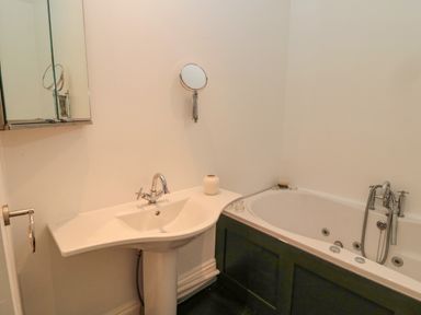 A bathroom with a sink and bathtub with faucets and a small round mirror on the wall at 2 The Reformed Church in Embleton
