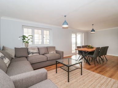 A living room with a gray sectional sofa a glass coffee table a dining table with six chairs and pendant lights at Rainbow View in Churchstanton near Churchinford