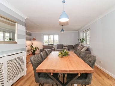 A dining room with a wooden table and gray chairs and a living area with gray sofas and plants at Rainbow View in Churchstanton near Churchinford