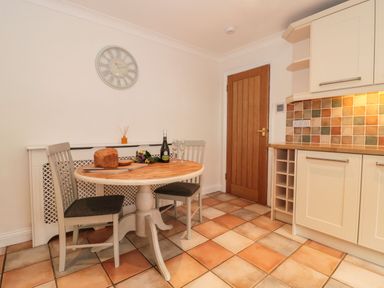 A kitchen with a round wooden table, two chairs, a loaf of bread, a bottle, two glasses, tiled floor and backsplash at Rainbow View in Churchstanton near Churchinford