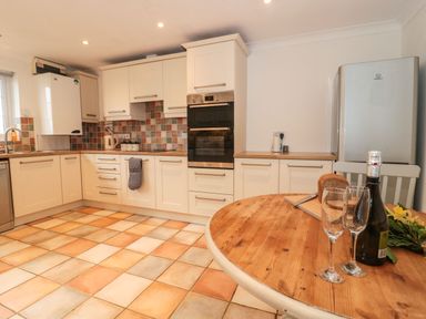 A kitchen with white cabinets tiled backsplash tiled floor and a wooden table with bread two glasses and a bottle at Rainbow View in Churchstanton near Churchinford