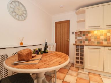 A kitchen with a round wooden table holding a loaf of bread champagne bottle and glasses at Rainbow View Churchstanton near Churchinford