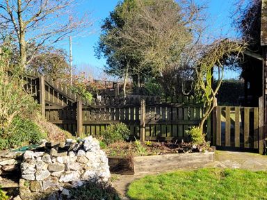 An outdoor garden area with a wooden fence and gate stone wall and a raised garden bed at Rainbow View in Churchstanton near Churchinford