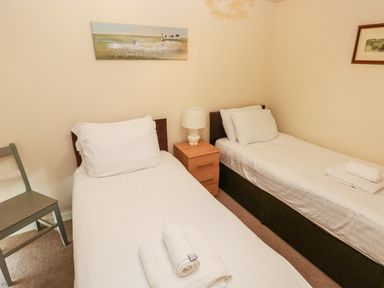 A bedroom with two single beds a small nightstand with a lamp and a chair at The Old Farm House in Redberth near Pentlepoir