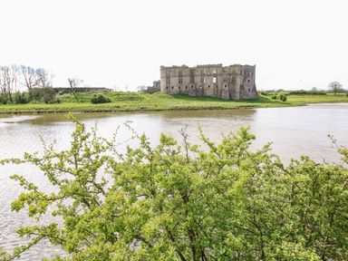 A river with green bushes in the foreground and an old stone castle on the opposite bank at The Old Farm House in Redberth near Pentlepoir