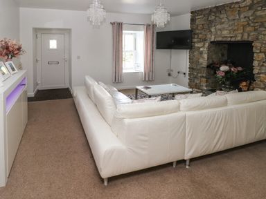 A living room with a white sofa stone fireplace and a wall mounted TV at The Old Farm House in Redberth near Pentlepoir