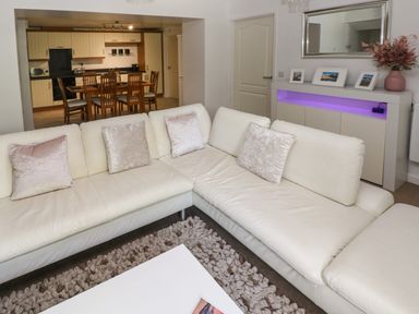 A living room with a white sectional sofa and a dining area with wooden table and chairs visible at The Old Farm House in Redberth near Pentlepoir