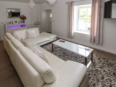 A living room with two white sofas a white coffee table and a cabinet with purple light at The Old Farm House in Redberth near Pentlepoir