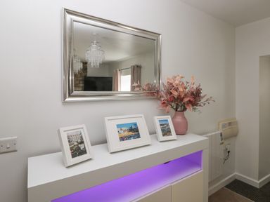 A white cabinet with three framed photos and a pink vase with flowers below a rectangular silver mirror at The Old Farm House in Redberth near Pentlepoir