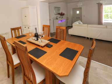 A dining area with a wooden table and six chairs with black placemats and glassware next to a white cabinet and a living room with a white sofa at The Old Farm House in Redberth near Pentlepoir