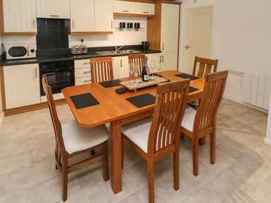 A dining table with six chairs and kitchen cabinets with countertop and appliances at The Old Farm House in Redberth near Pentlepoir
