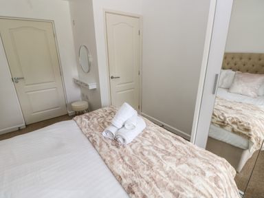 A bedroom with a bed covered with a patterned blanket and towels on top two doors a round mirror and a stool at The Old Farm House in Redberth near Pentlepoir