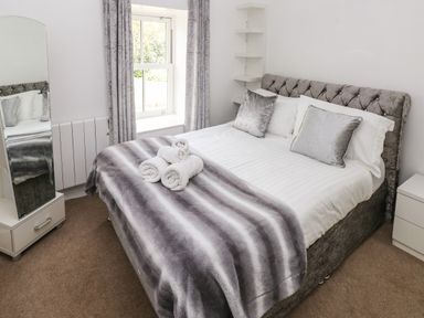 A bedroom with a double bed a mirror a window with curtains and rolled towels on the bed at The Old Farm House in Redberth near Pentlepoir