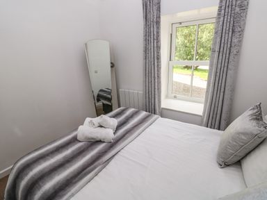 A bedroom with a bed covered by a blanket and pillows a mirror near a window with curtains at The Old Farm House in Redberth near Pentlepoir