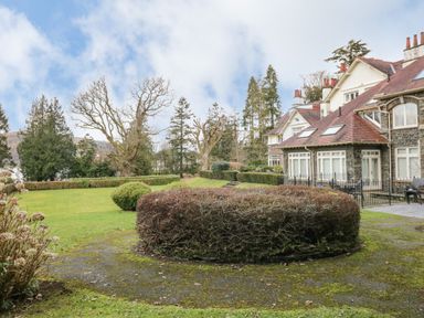 A garden with trimmed bushes and trees beside a large stone and brick house at Lake House Loft in Bowness-On-Windermere
